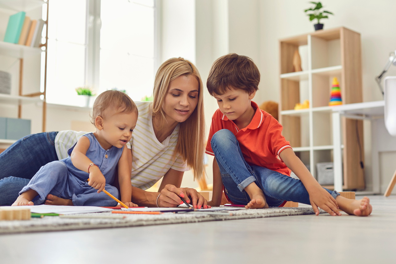 Young Mommy and Children Drawing Picture Together Sitting on Floor in Nursery